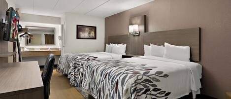 A hotel room with two beds, a desk, a chair, a mirror, and a wall-mounted TV.