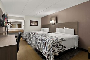 Una habitación de hotel con dos camas, un escritorio, una silla, un espejo y un televisor montado en la pared.