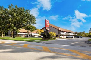 Un Red Roof Inn con un cielo azul despejado, un estacionamiento y una zona verde con árboles.