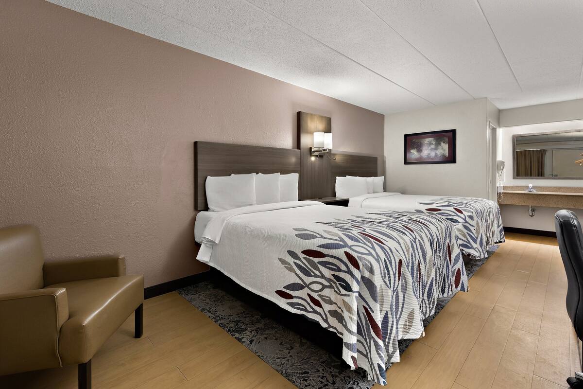 A hotel room with a large bed, a chair, a desk, and a mirror.