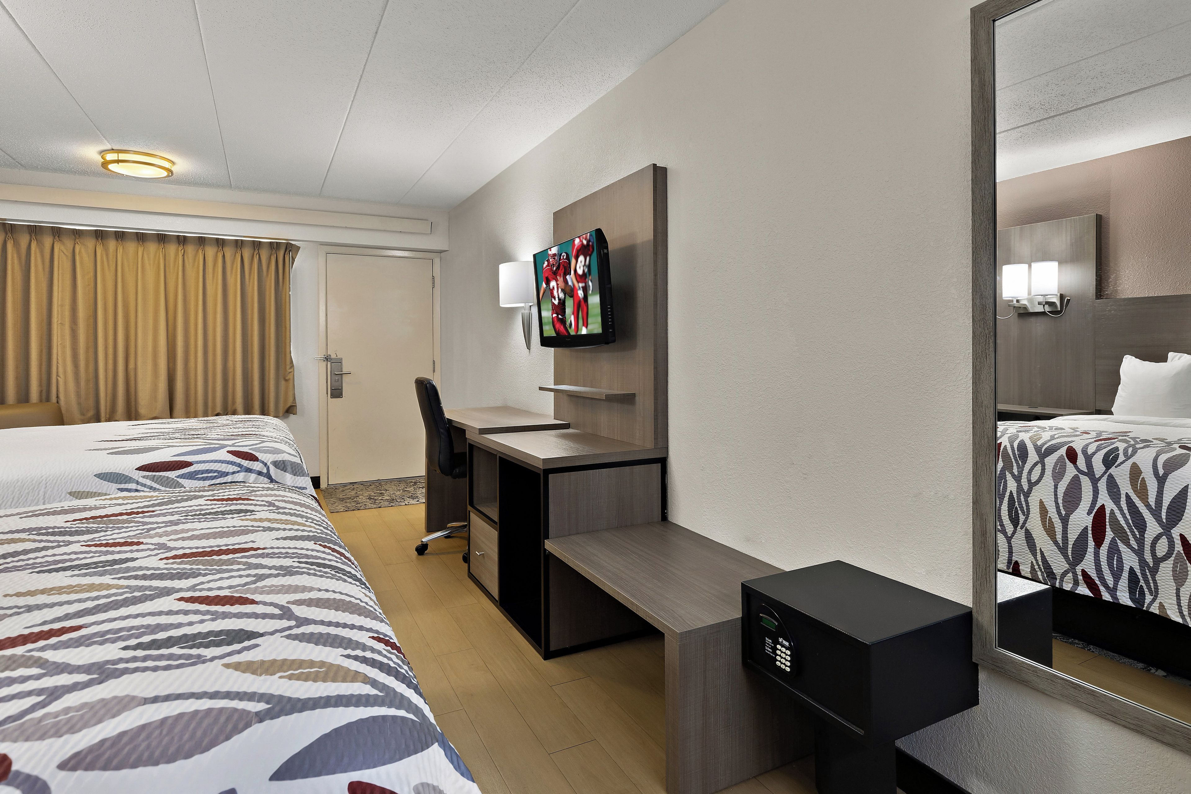 A hotel room with a bed, desk, chair, TV, and a mirror.