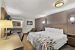 A hotel room with a bed, bedside tables, a desk, a chair, a mirror, and a wall-mounted light fixture.