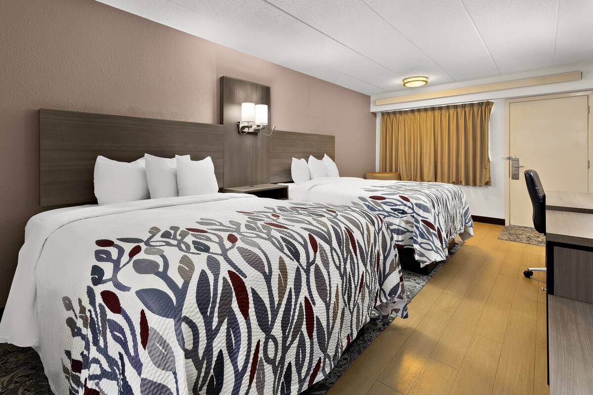 A hotel room with two beds, a desk, and a chair.