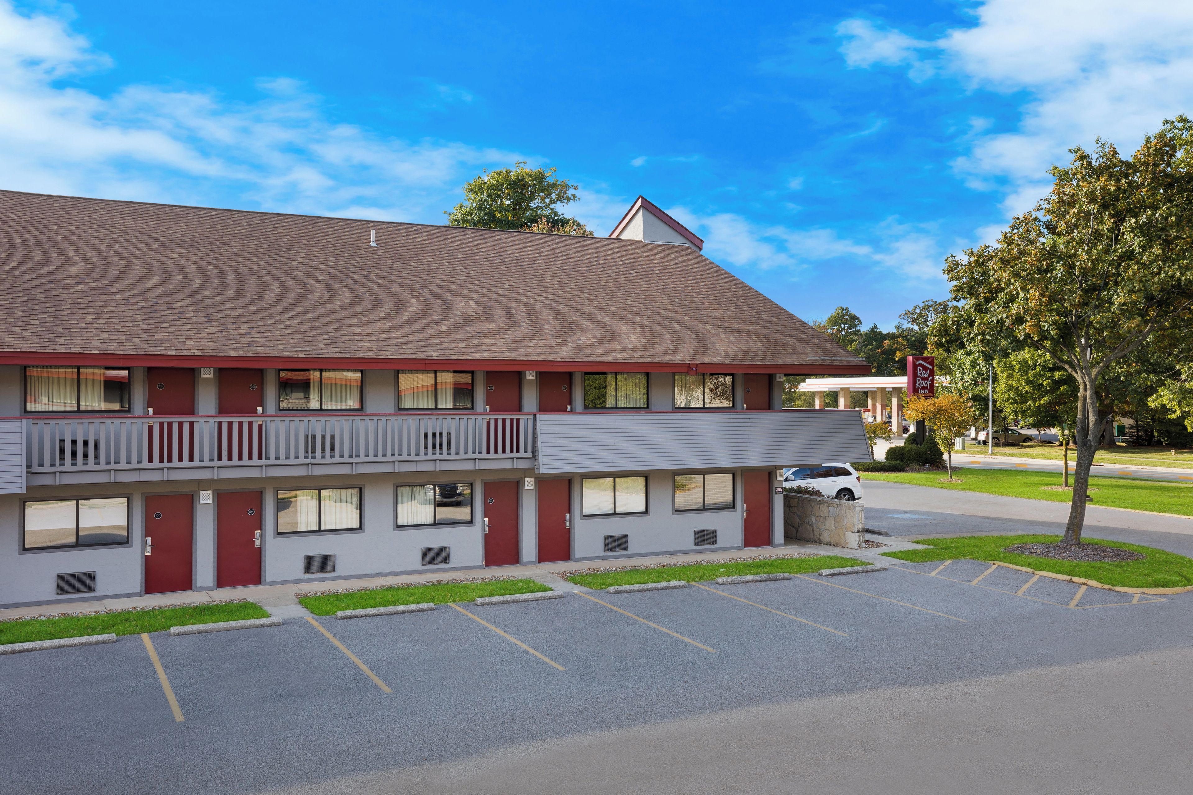 Un motel de dos pisos con fachada roja y gris, un estacionamiento y un árbol en la parte delantera.