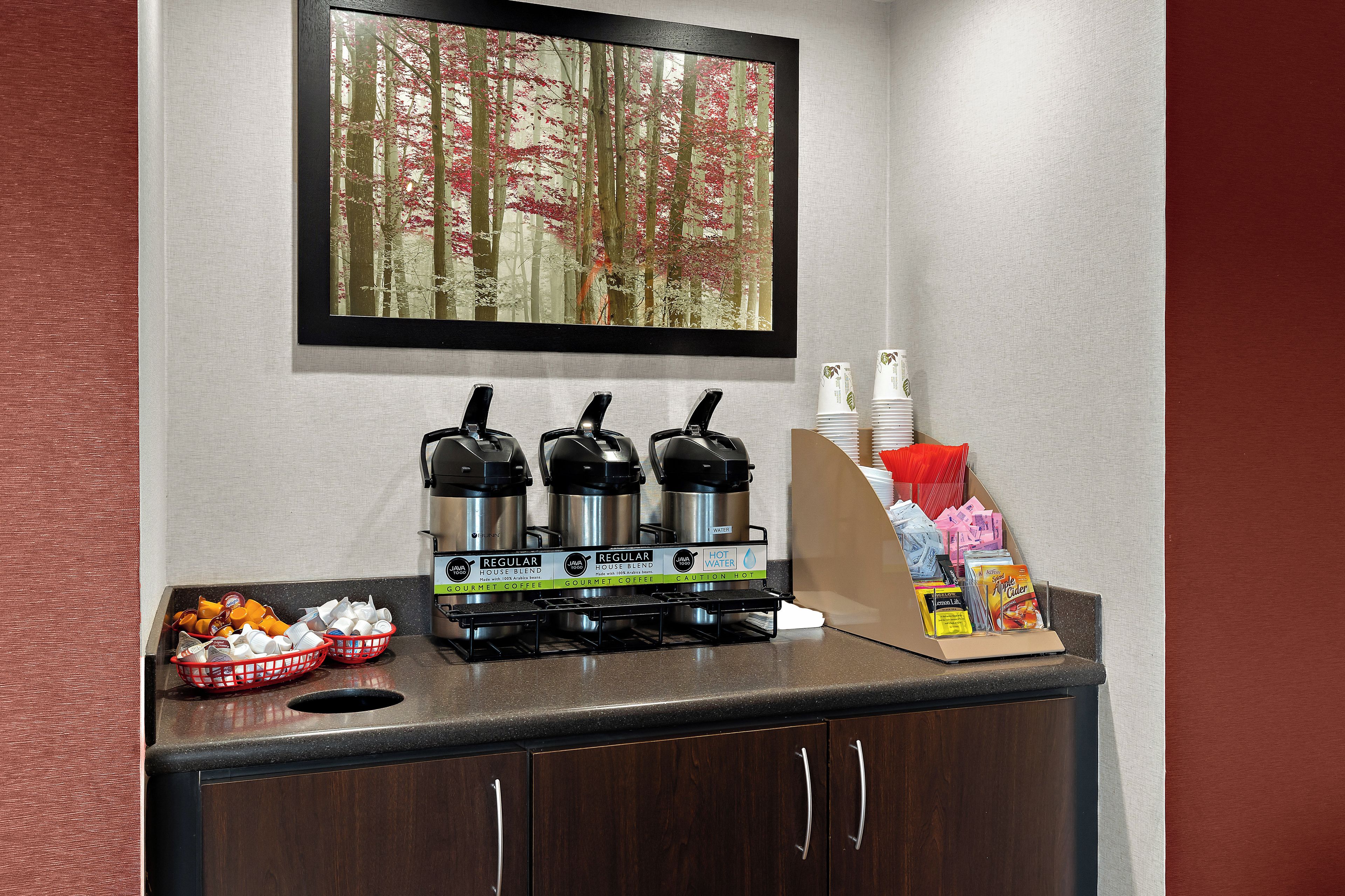 A coffee station with three coffee makers, a water dispenser, and a display of coffee pods and cups.
