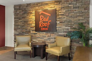 Vestíbulo de Red Roof Inn con pared de piedra, dos sillones de cuero, una mesita redonda y una planta en maceta.