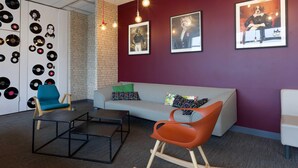 A modern interior with a brick wall, a grey sofa, a blue chair, and a red rocking chair. There are framed pictures on the wall and vinyl records on the left. - B&B Hotel Reims Centre Erlon (Reims)