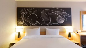 A hotel room with a large abstract painting on the wall, two bedside lamps, a neatly made bed, and a wooden nightstand. - B&B Hotel Reims Centre Erlon (Reims)