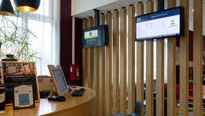 A reception desk with a computer, a monitor displaying WiFi information, a plant, and a fire extinguisher. - B&B Hotel Reims Centre Erlon (Reims)