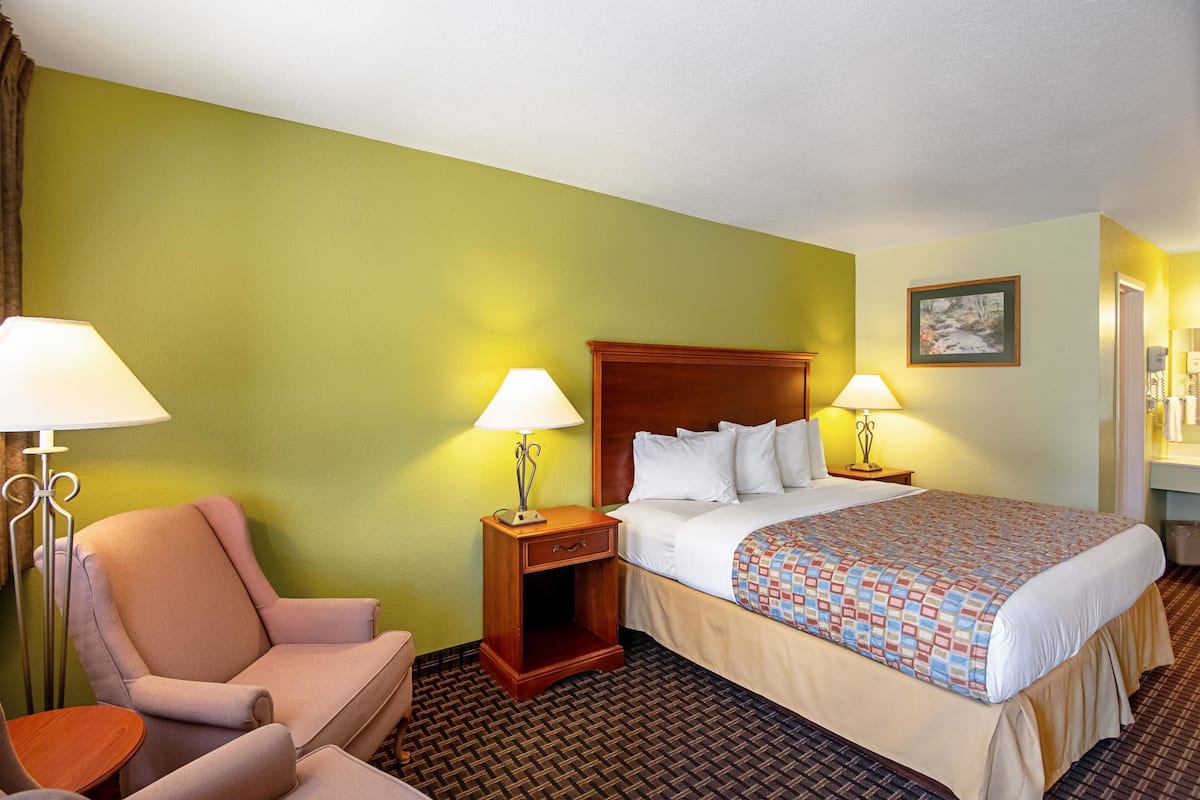 Une chambre d’hôtel avec un lit, deux tables de chevet avec des lampes, une chaise et une petite table.