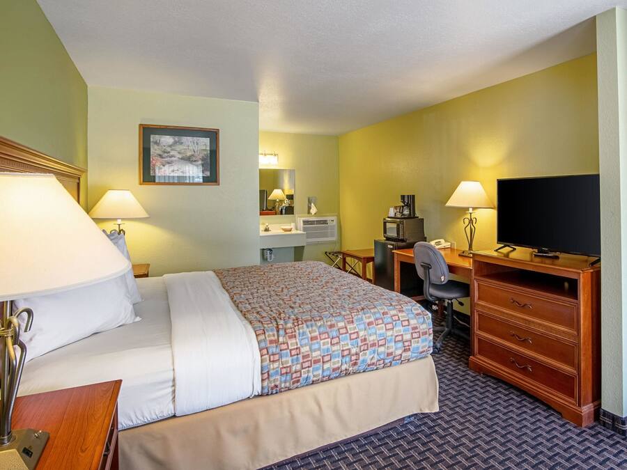 A hotel room with a bed, desk, chair, television, and a desk lamp.