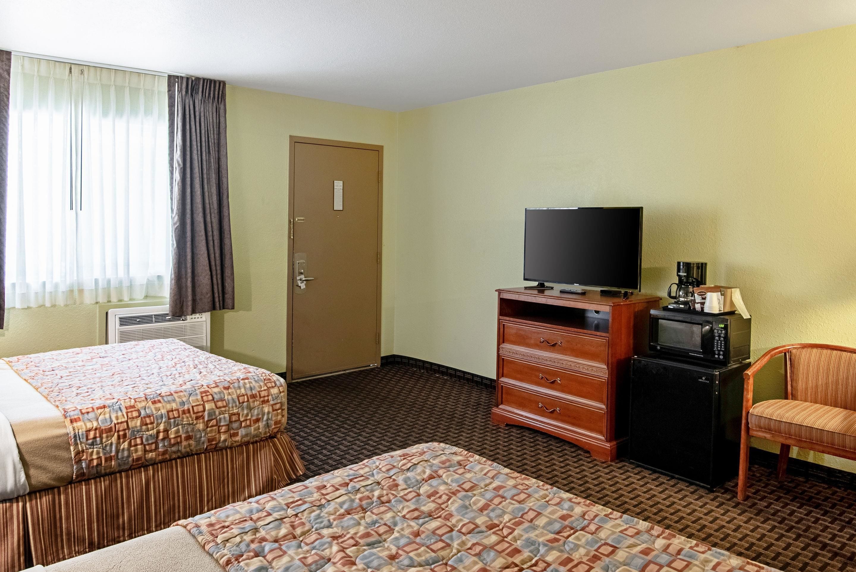 Quarto de hotel com duas camas, televisão, cômoda e uma cadeira.