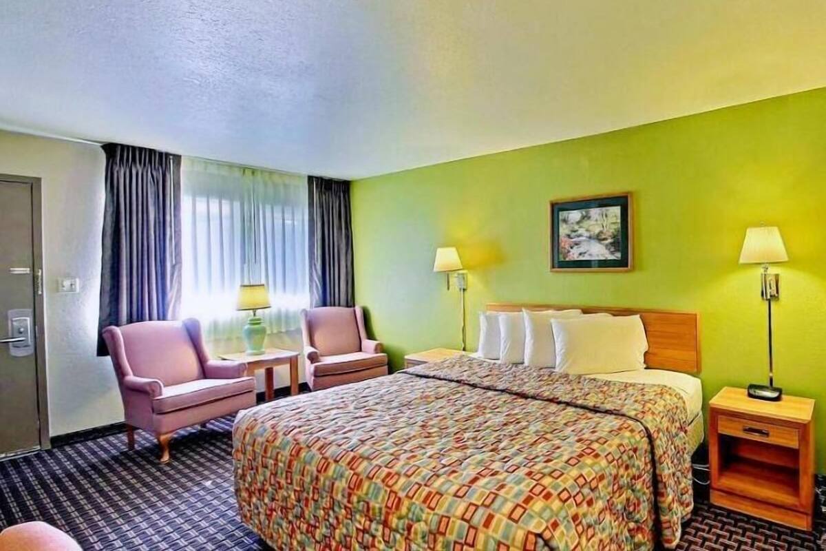 Une chambre d’hôtel avec un lit, deux chaises, un bureau, une table de chevet et une lampe.