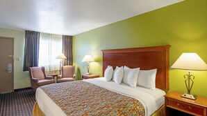 Ein Hotelzimmer mit einem großen Bett, zwei Nachttischen mit Lampen, einem Sessel und einem Schreibtisch.