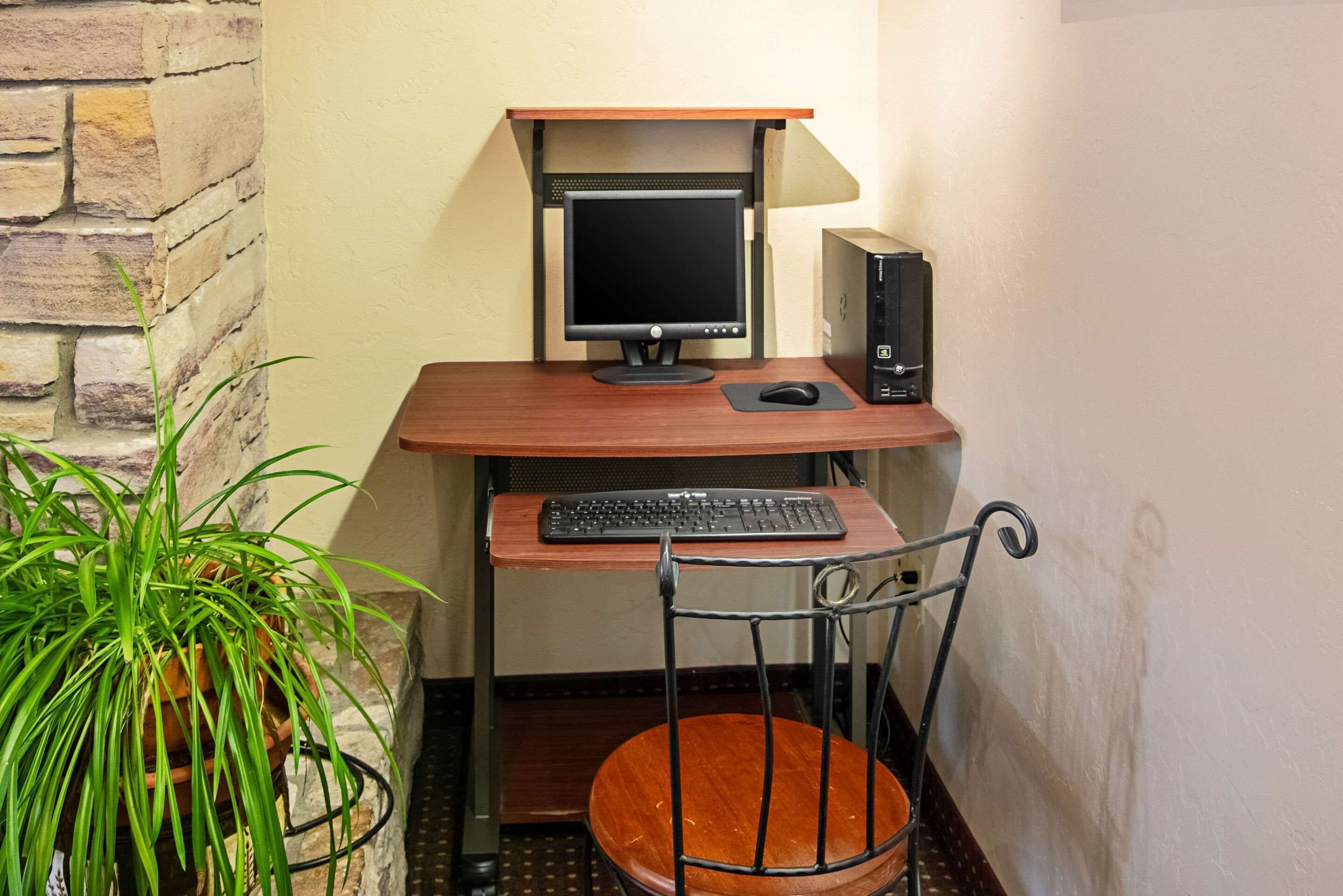 A small office space with a desk, computer, keyboard, and chair. There is a potted plant on the left.