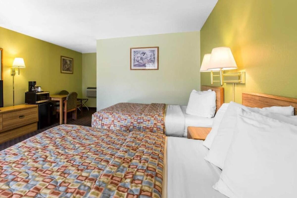 Une chambre d’hôtel avec deux lits, un bureau, une chaise, une lampe et un tableau au mur.