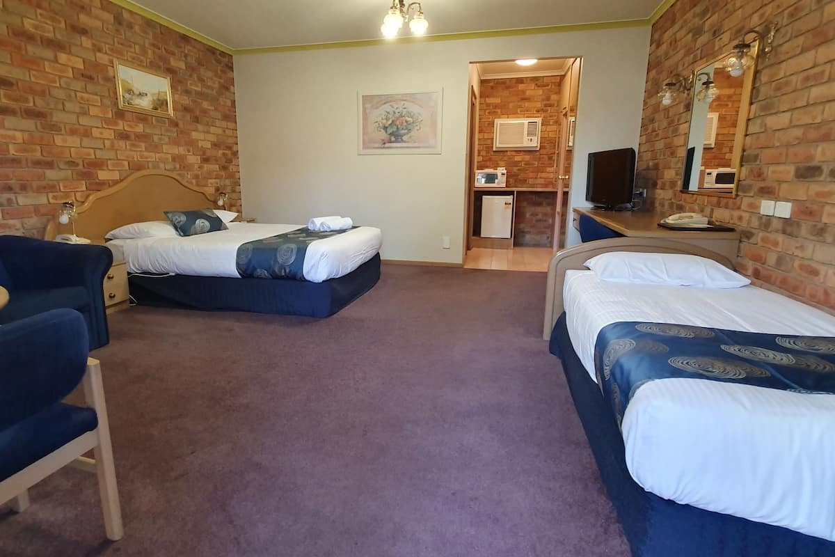 A hotel room with two beds, a desk, a chair, and a small kitchenette.