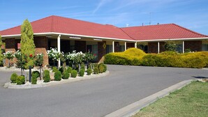 A two-story building with a red roof, a brick facade, and a landscaped front yard with various shrubs and small trees. - Pines Country Club Motor Inn (Shepparton)