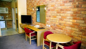 A room with a brick wall, a wooden desk, a television, a mirror, and two red chairs. - Pines Country Club Motor Inn (Shepparton)