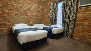 A room with two beds, a brick wall, a window with patterned curtains, and a carpeted floor. - Pines Country Club Motor Inn (Shepparton)