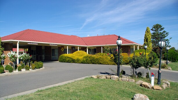 A two-story building with a red roof, a covered entrance, and a landscaped front yard with bushes and a small tree.