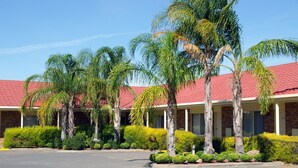 A hotel with a red-tiled roof, palm trees, and a parking lot.