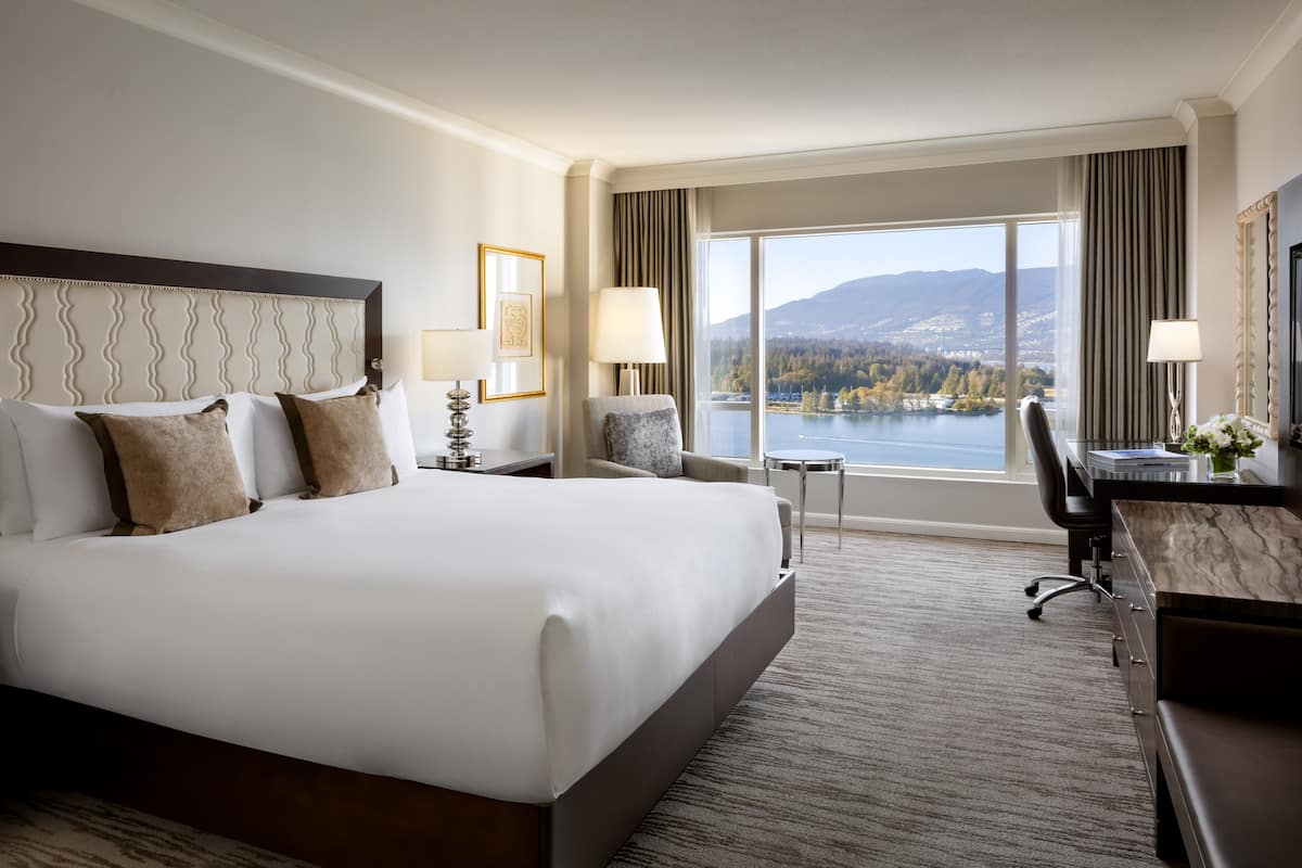 A hotel room with a large bed, a desk, a chair, and a view of a lake and mountains.