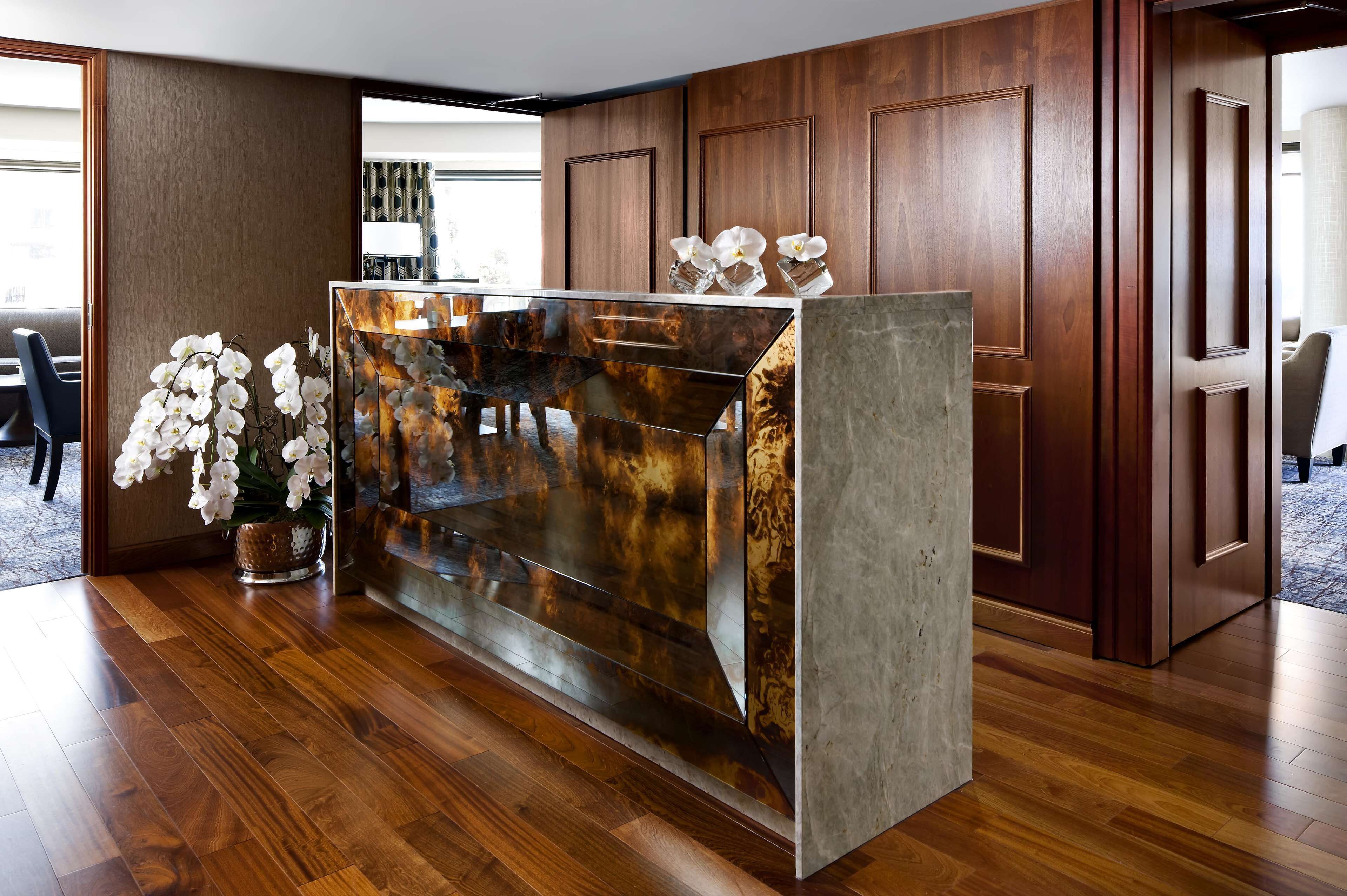 A reception desk with a marble top, surrounded by wooden paneling and a potted orchid plant.
