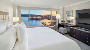 Quarto de hotel com uma cama grande, uma escrivaninha com televisão, uma cadeira e vista para um porto com guindastes.