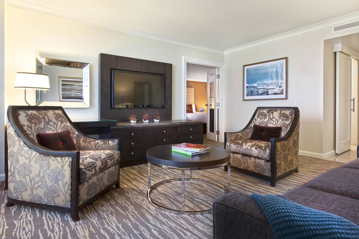 A hotel room with two armchairs, a sofa, a coffee table, a TV, a dresser, and a painting on the wall.