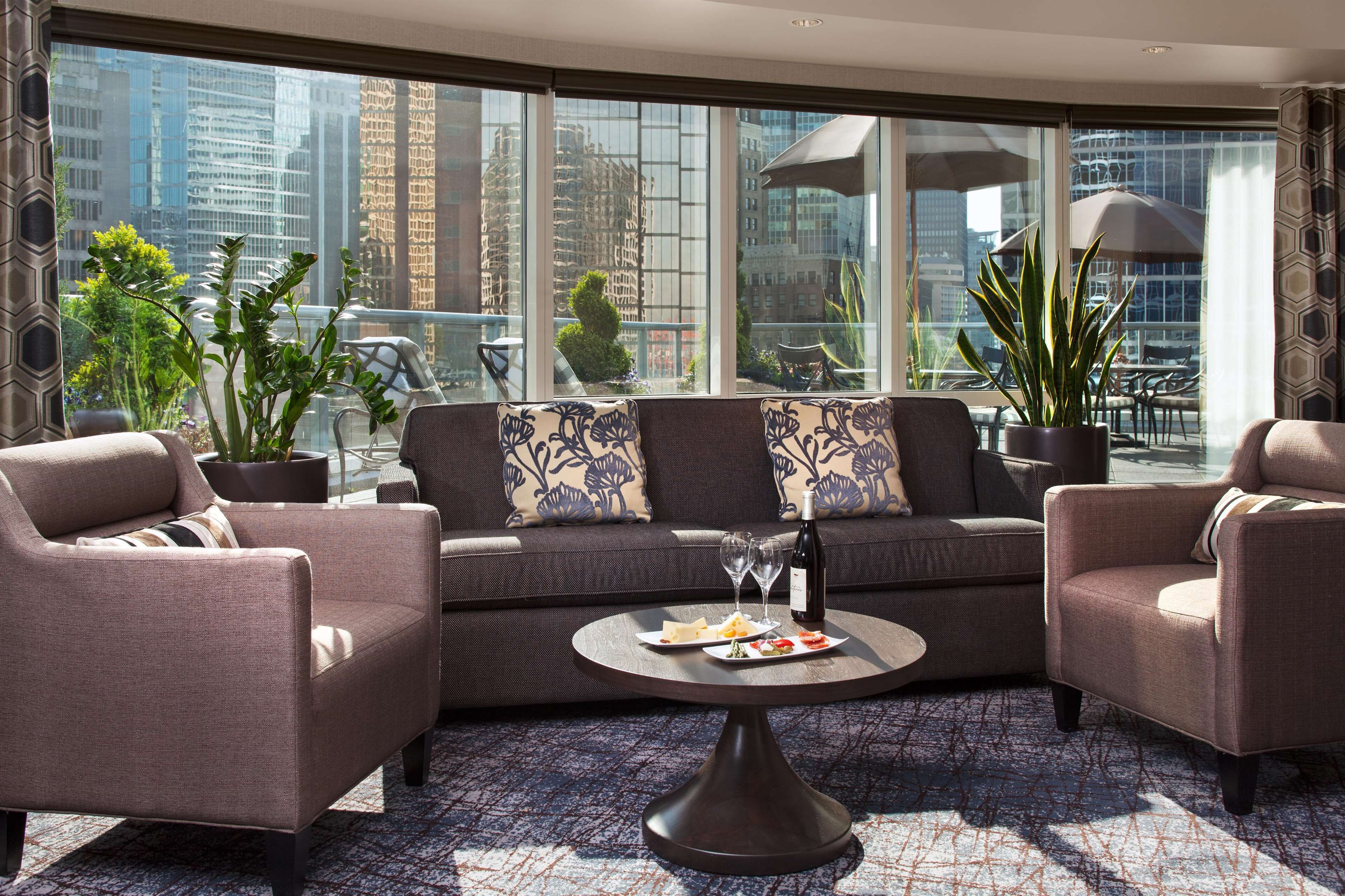 A modern living room with a sofa, two armchairs, a coffee table, and a large window offering a city view.