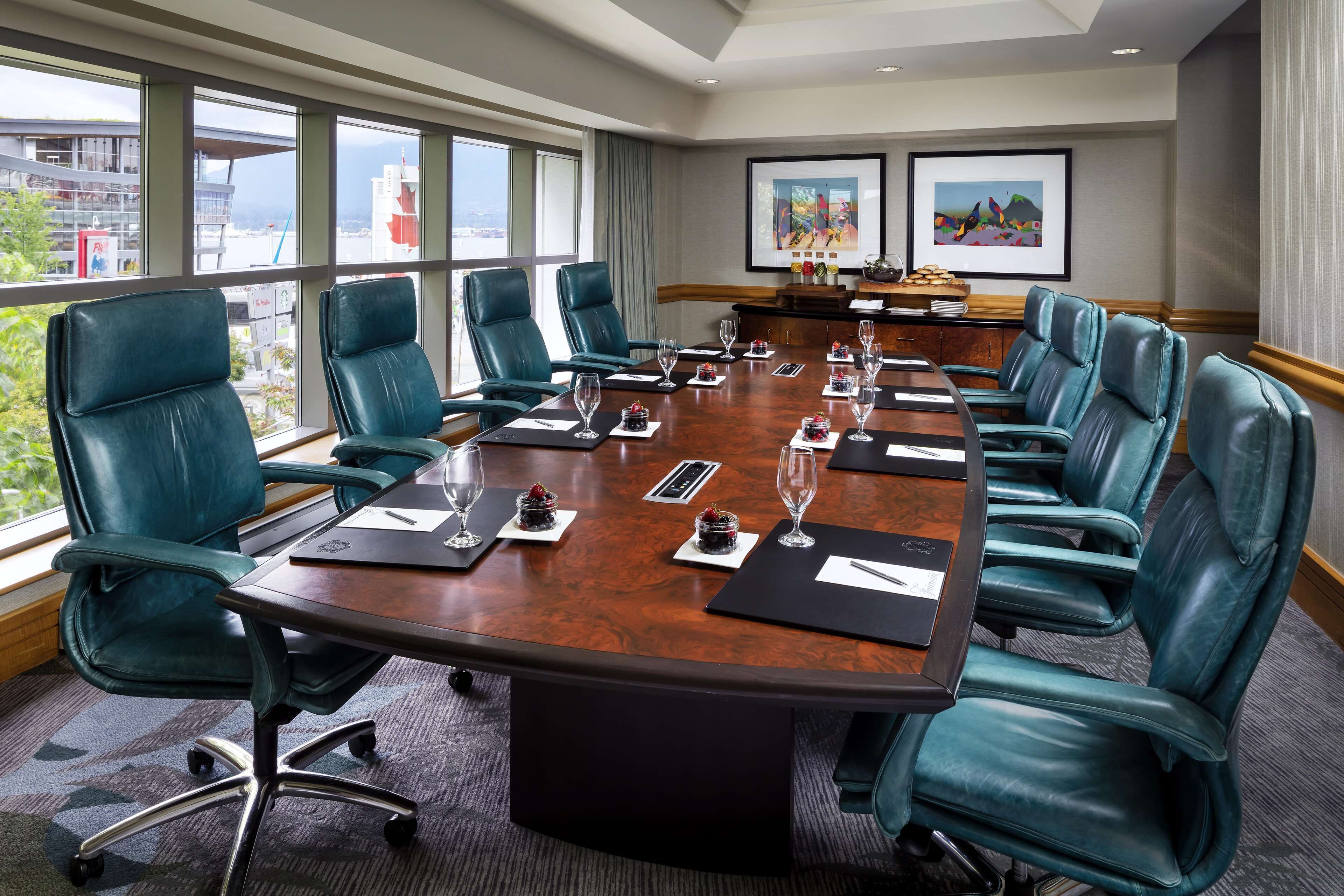A conference room with a large table, teal leather chairs, and large windows offering a view of buildings and greenery.