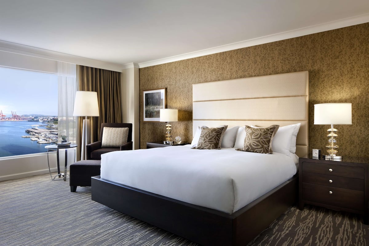 A hotel room with a large bed, two bedside tables, a chair, and a view of the water.