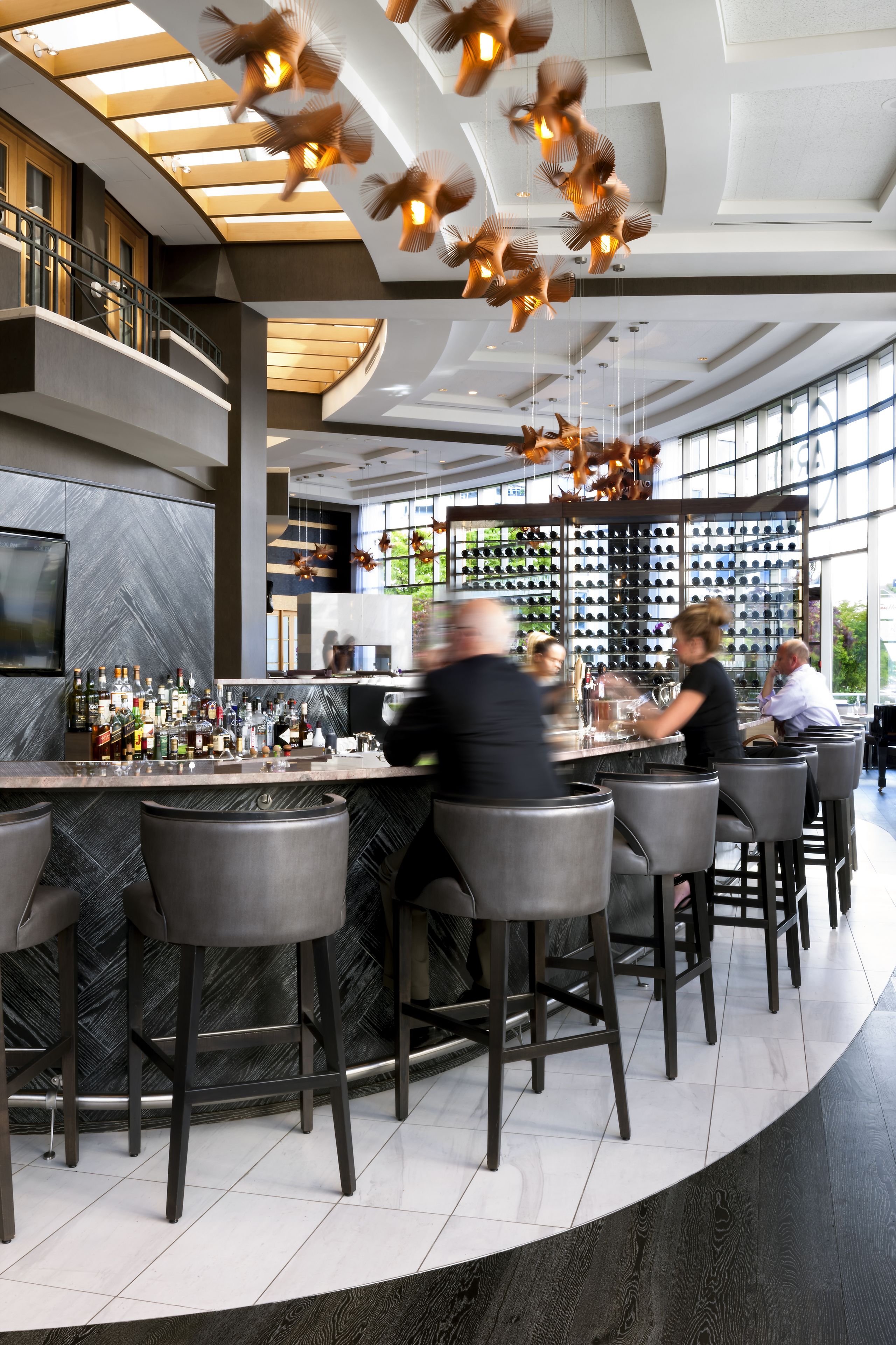 Un área de bar moderna con una barra curva, taburetes y una estantería para vinos al fondo.