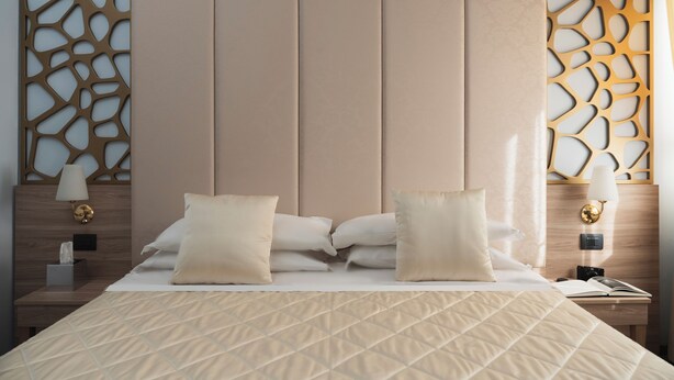 Una habitación de hotel con una cama grande, dos mesitas de noche, una lámpara de pared y un panel decorativo.