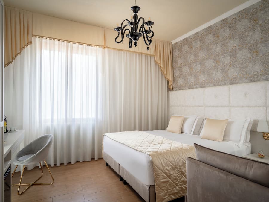A hotel room with a bed, a chair, a desk, and a chandelier.