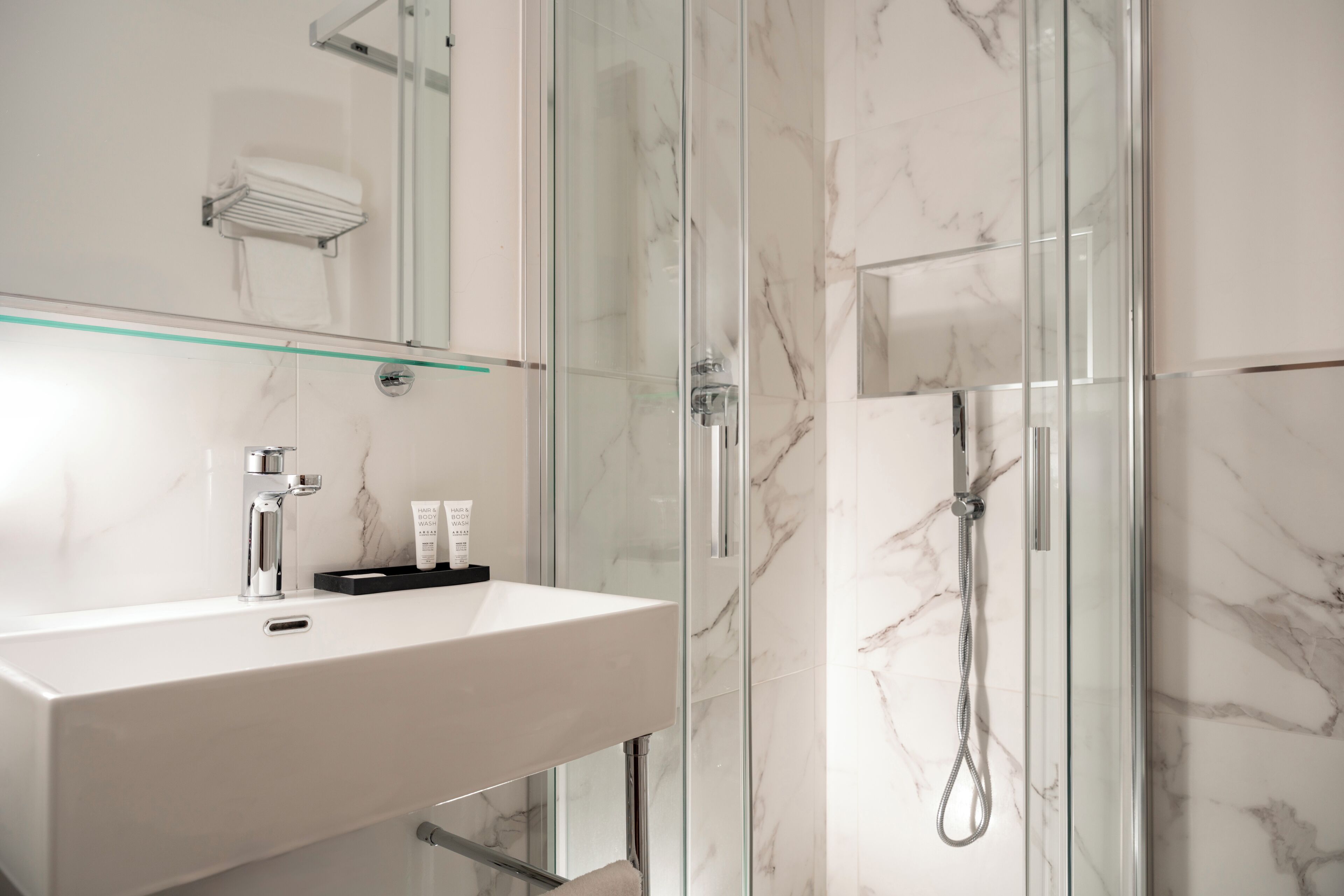 Un baño moderno con cabina de ducha de vidrio, un lavabo blanco y un espejo sobre él.