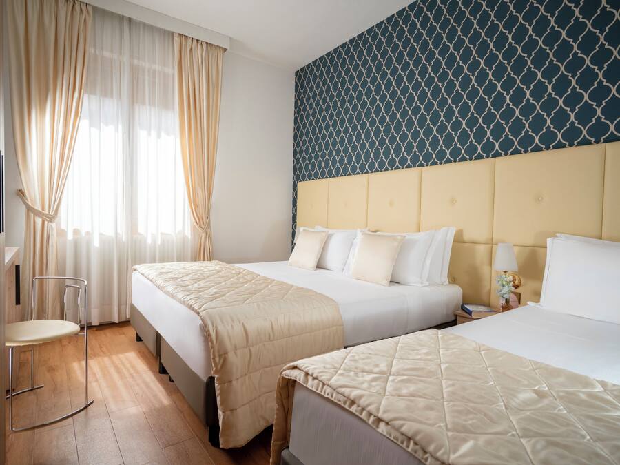 A hotel room with two beds, a bedside table, a chair, and a patterned wall.