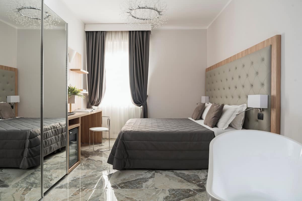 A modern hotel room with two beds, a desk, and a chair.
