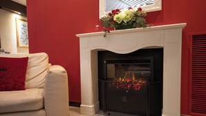 Una habitación con chimenea blanca, pared roja y sofá blanco con un cojín rojo.
