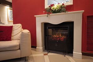 Una habitación con chimenea blanca, pared roja y sofá blanco con un cojín rojo.