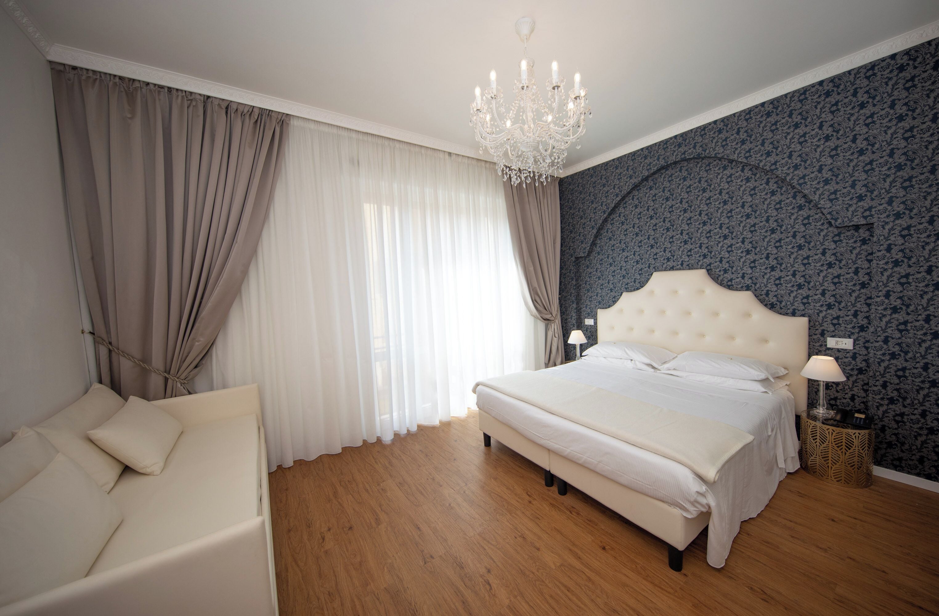 Een slaapkamer met een groot bed, een kroonluchter, een nachtkastje en een bank.