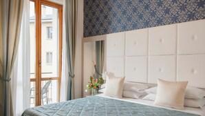 Una cama bien hecha con colcha acolchada, cabecera con paneles capitonados y un florero con flores en la mesita de noche.