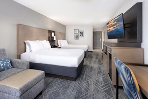 A hotel room with a large bed, a smaller bed, a sofa, a desk, a TV, and a bathroom.