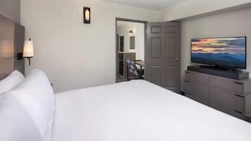 A hotel room with a large bed, a television on a dresser, a door leading to a bathroom, and a wall-mounted light fixture.