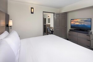 A hotel room with a large bed, a television on a dresser, a door leading to a bathroom, and a wall-mounted light fixture.