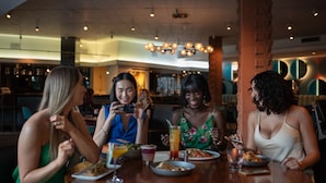A group of people dining at a restaurant with a modern interior, including a brick column and pendant lighting. - Hotel Valley Ho (Scottsdale)
