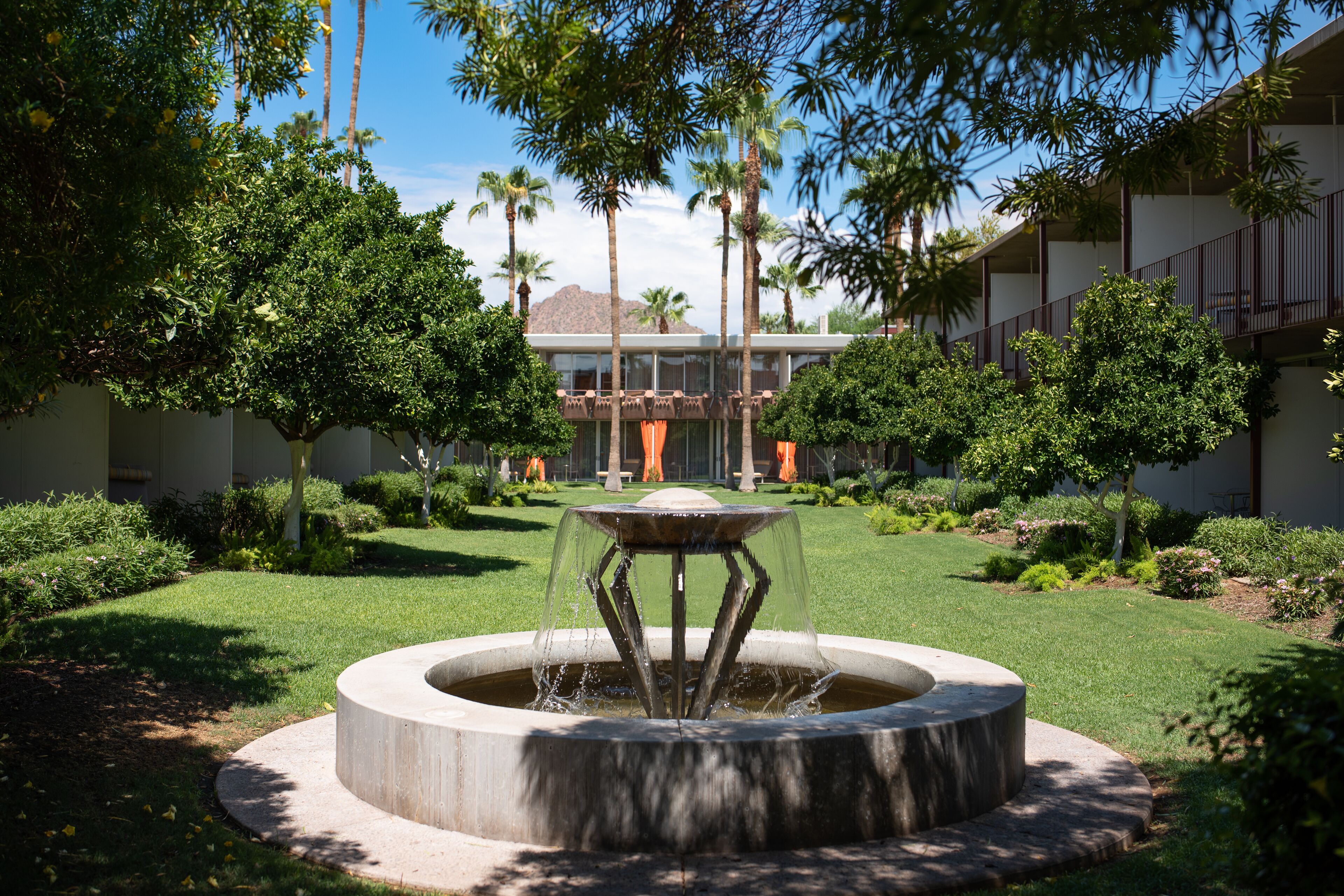 A courtyard with a central fountain, surrounded by well-maintained grass and various trees.