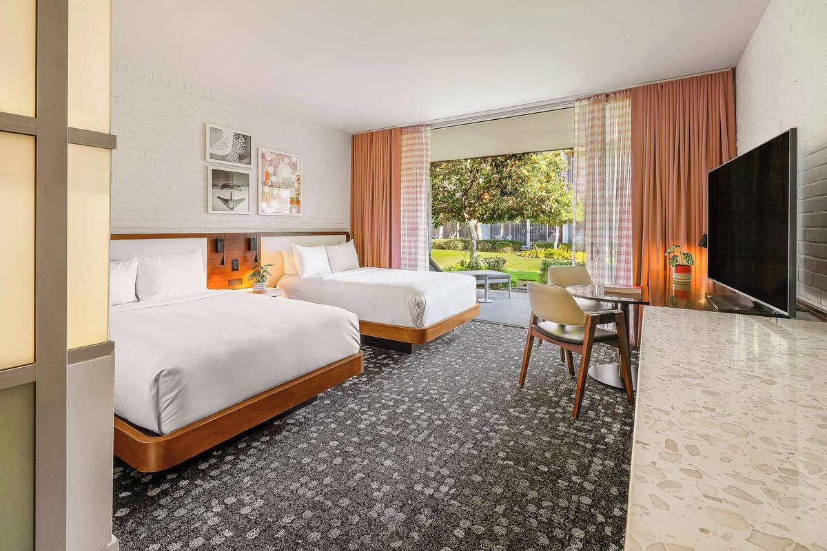 A hotel room with two beds, a TV, a dining table with chairs, and a view of the outdoors.