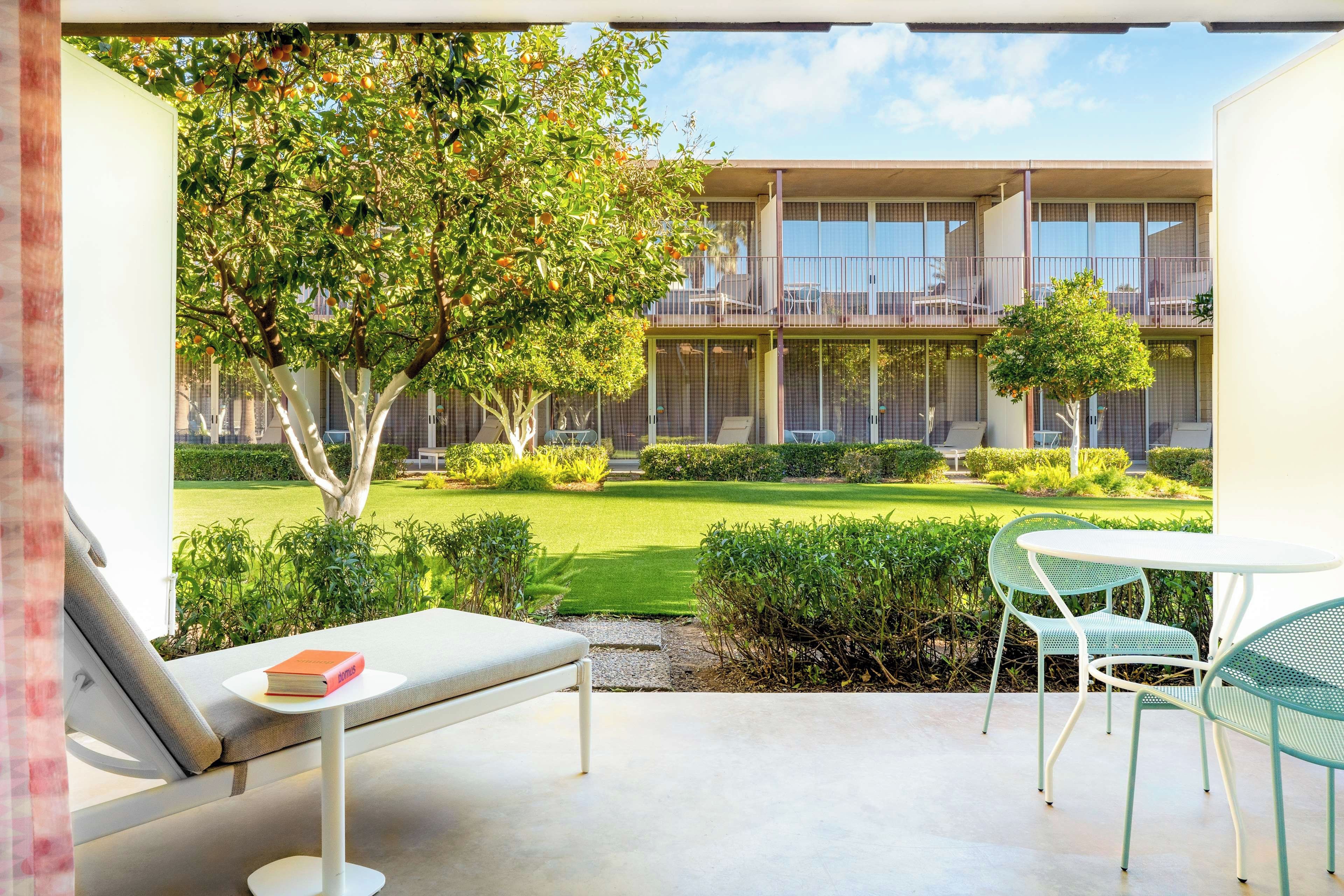 A balcony with a sofa and chairs, overlooking a well-maintained garden and a building with multiple balconies.